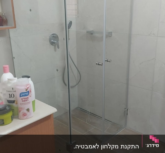 מקלחון זכוכית בחדר אמבטיה עם מוצרי טיפוח על מדף